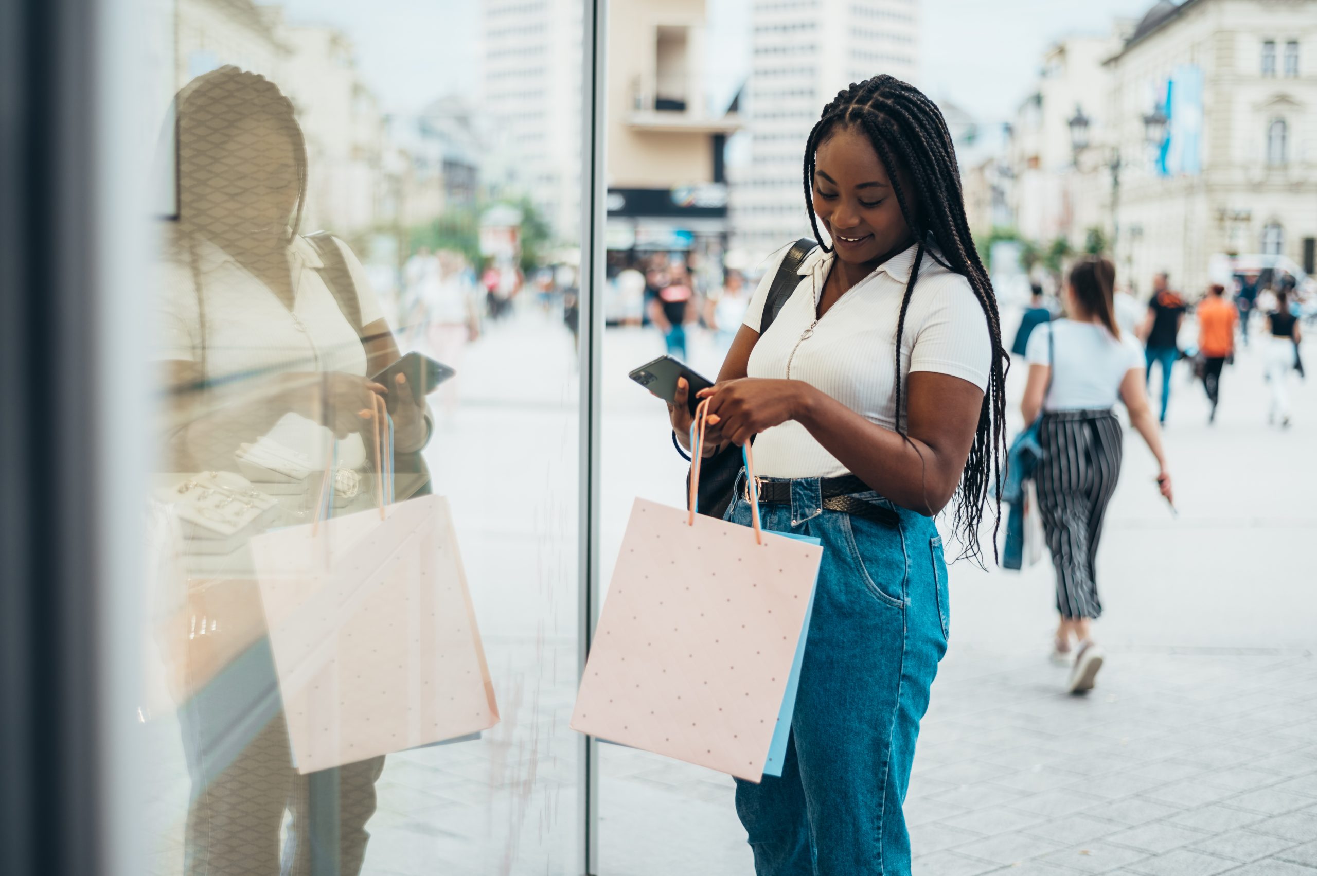 Beautiful african american woman holding shopping bags and using smartphone while out in the city on a summer day